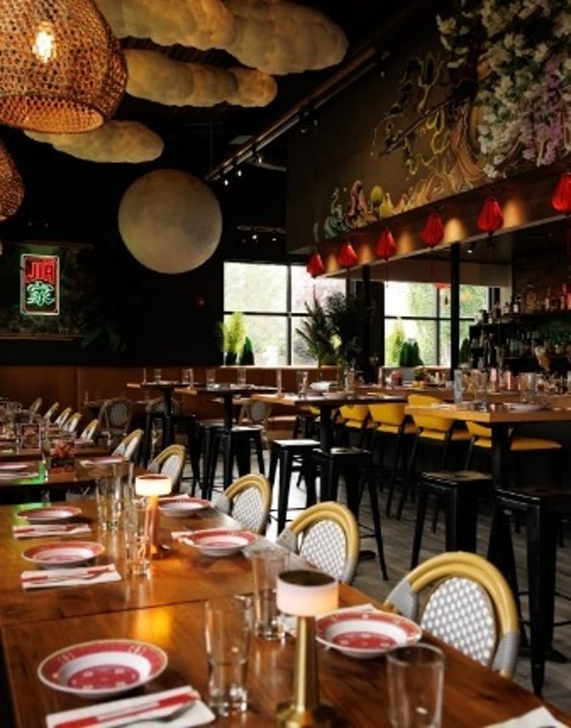 Modern restaurant interior with long wooden tables, cloud-like ceiling decor, and a large moon art piece.