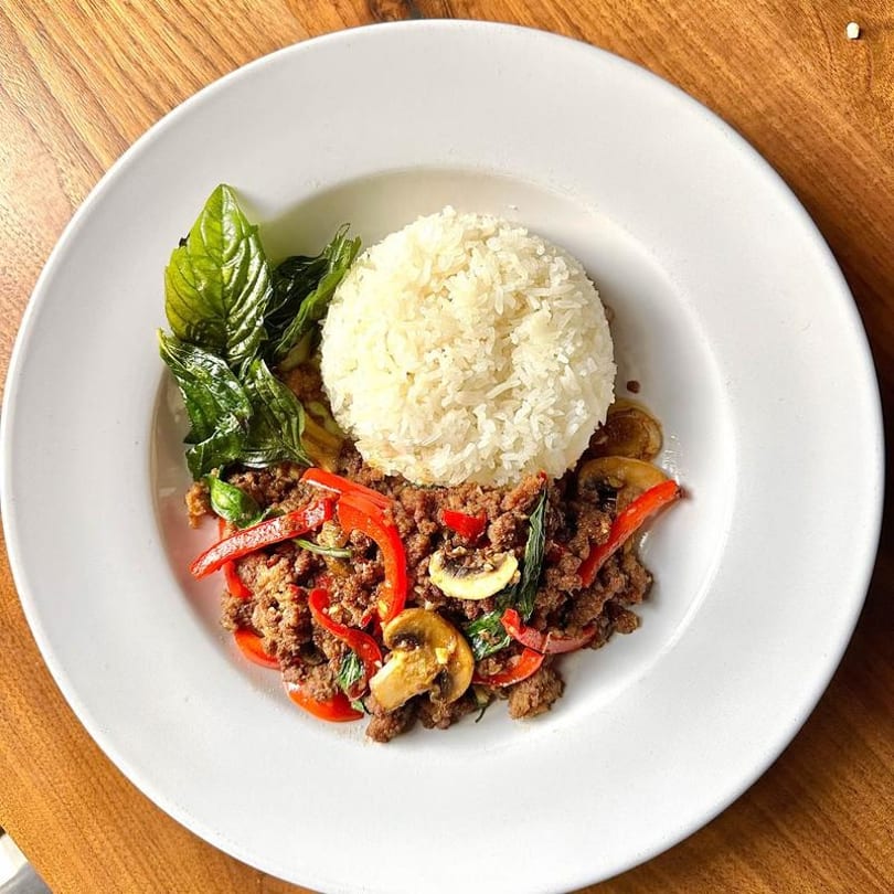 Thai basil beef with red peppers, mushrooms, and rice on a white plate.