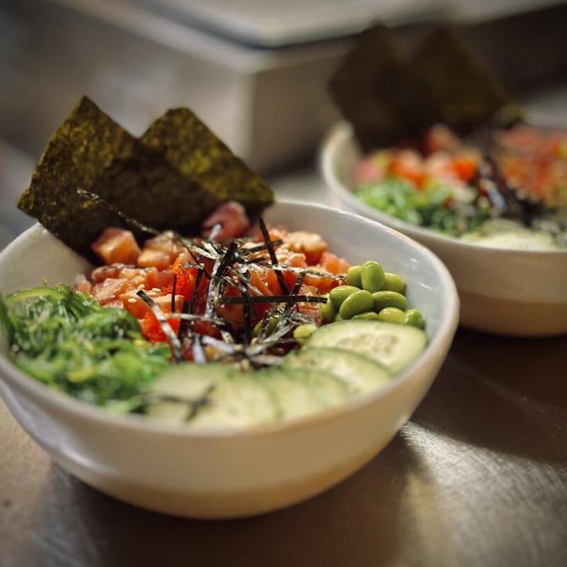 Two colorful poke bowls with salmon, seaweed, edamame, and cucumber slices.